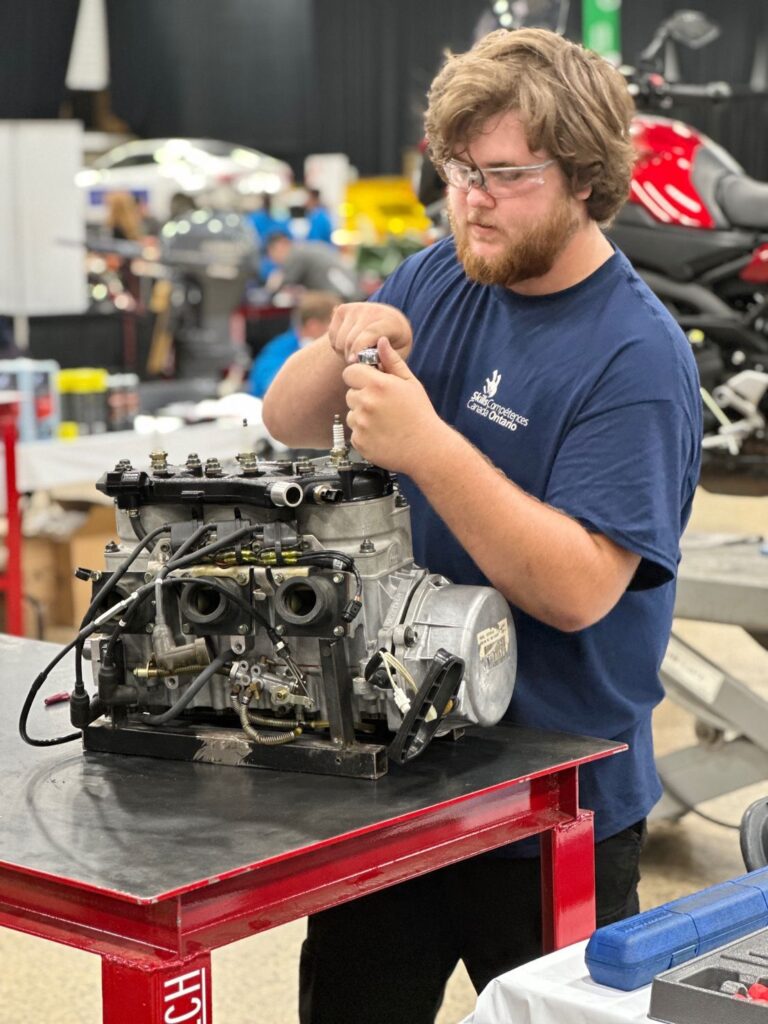 A person wearing a blue shirt with safety glasses working on a small engine.