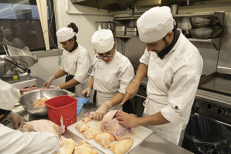 Three people wearing white chef uniforms chopping up turkey pieces in a large kitchen