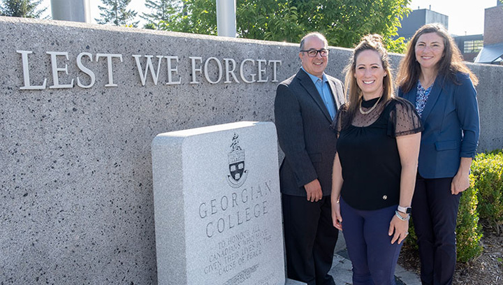 Brian Muscat, Joanna Coulthard and Rebecca Sabourin in business attire standing outside beside the cenotaph at the Georgian College Barrie Campus