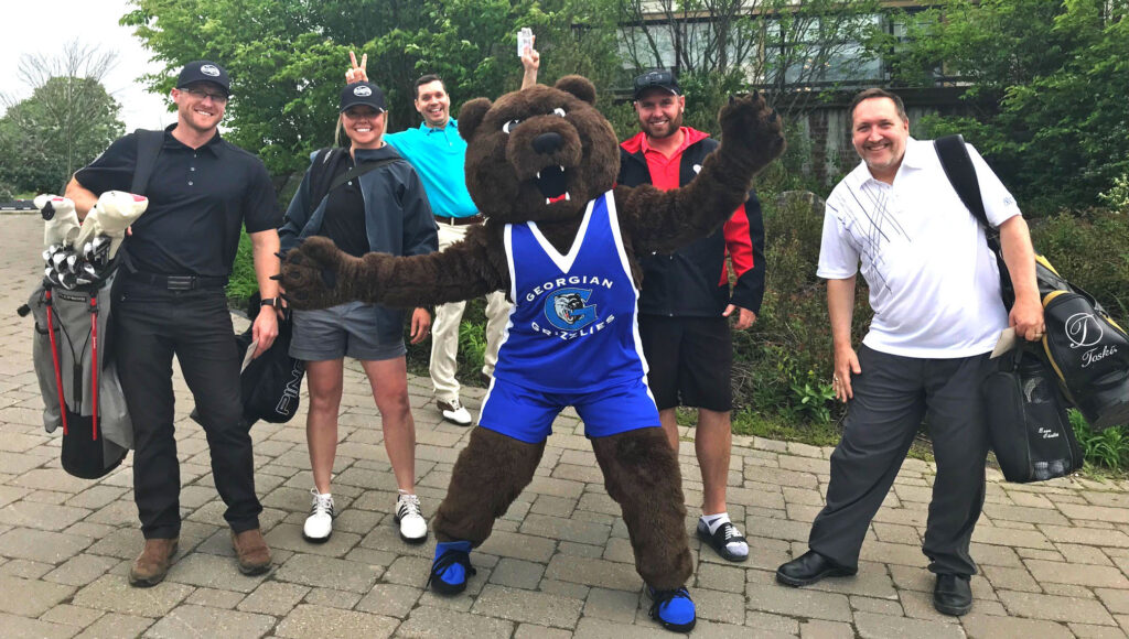Several golfers smiling and posing with Georgian mascot Growler at the 2022 Georgian Golf Classic event