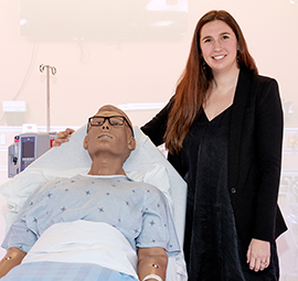 Woman stands beside a manikin in a hospital bed.
