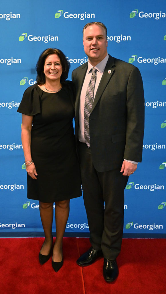 A man (Kevin Weaver) and a woman (Giselle Bodkin) smiling and dressed in business attire. They're standing in front of blue background with the Georgian logo on it.