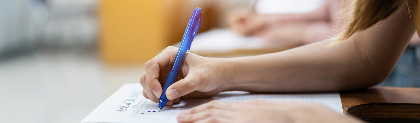 Close up of female college student hand writing exam answer in the classroom.