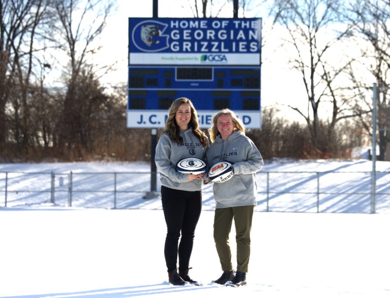 Two people standing in a snowy field with rugby balls.