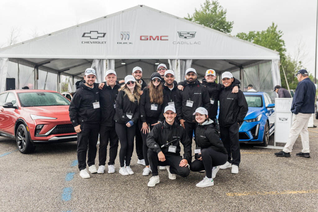 Team of students standing in front of a display of cars and tent