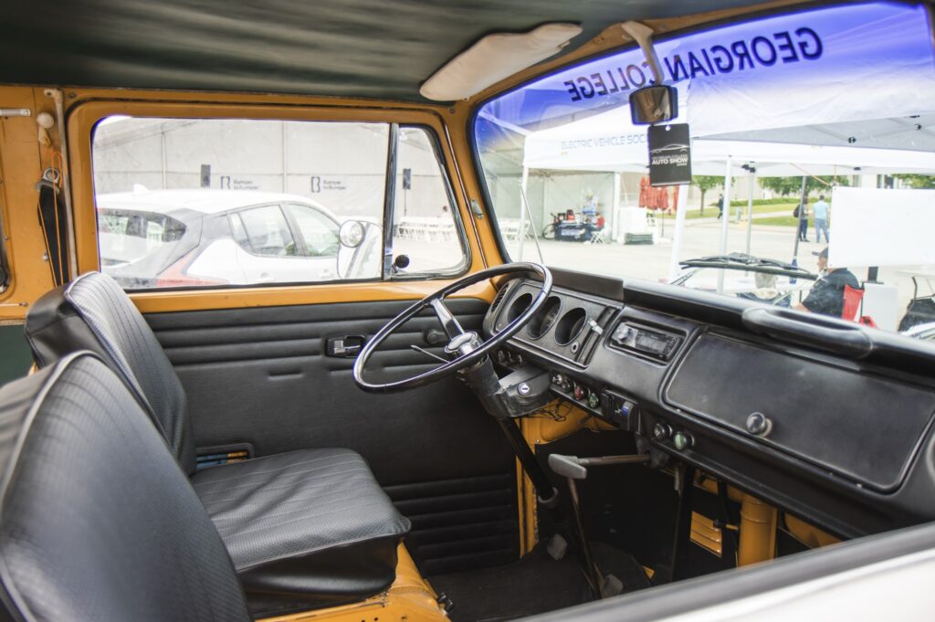 The interior of the driver's and passenger seats, steering wheel and dashboard of a vehicle. Text at the top of the windshield reads "СŶƵ."