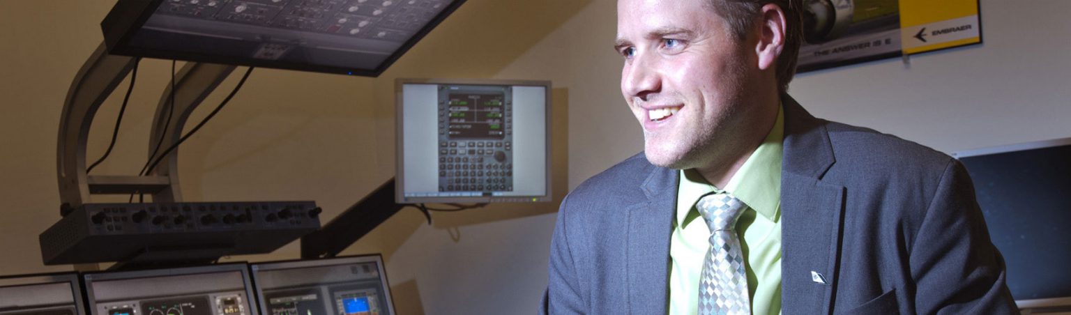 Aviation industry professional wearing a suit and tie while smiling next to flight simulator equipment