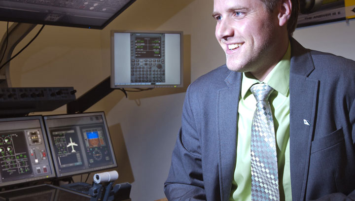 Aviation industry professional wearing a suit and tie while smiling next to flight simulator equipment