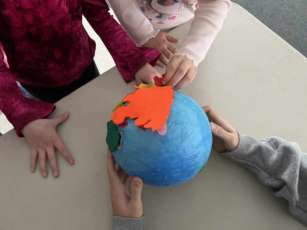 Three children playing with a blue globe with felt pieces stuck on it representing the different countries.