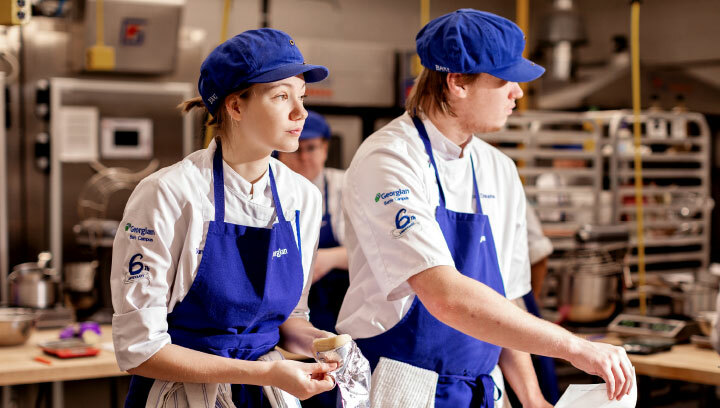 Georgian College Baking and Pastry arts students wearing uniforms, aprons, hair nets and hats making pastry in the baking lab