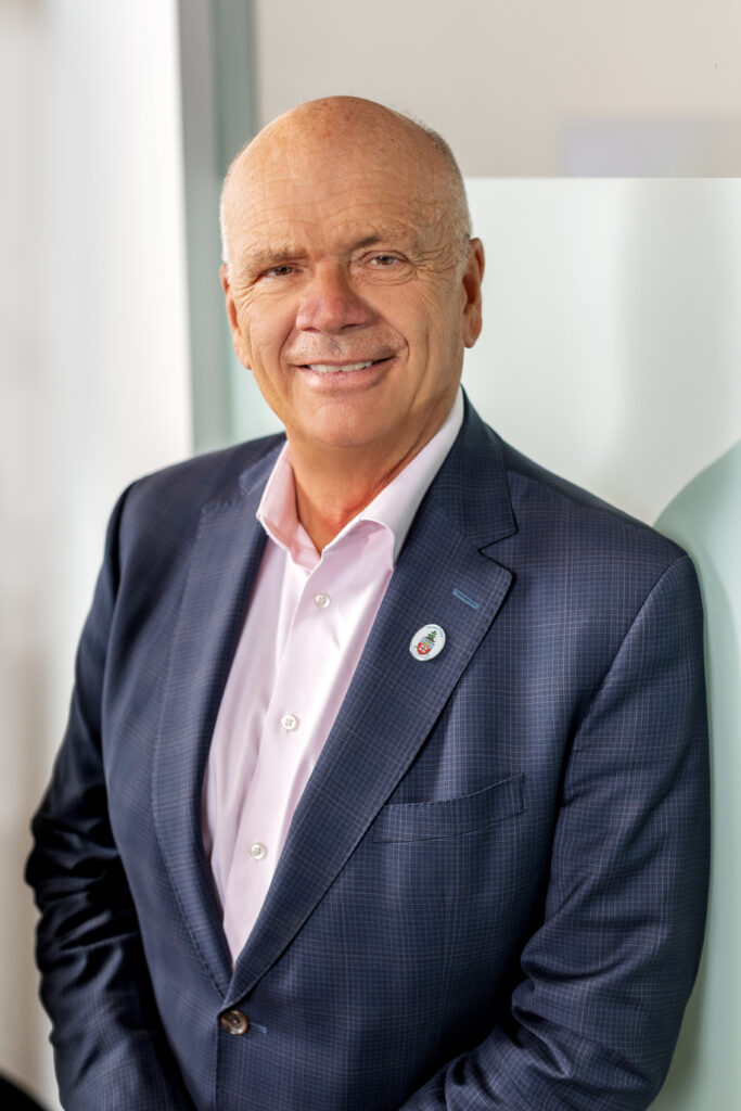 A headshot of a person wearing a blue suit and pink dress shirt. 