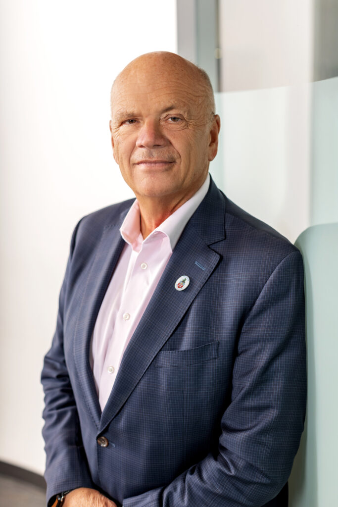 A headshot of a person standing and who's wearing a blue blazer and pink dress shirt.