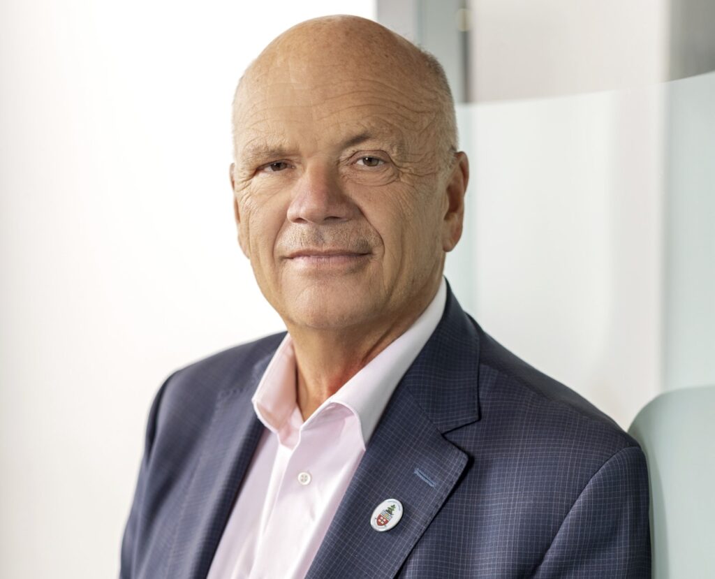 A headshot of a person wearing a blue blazer and pink shirt.