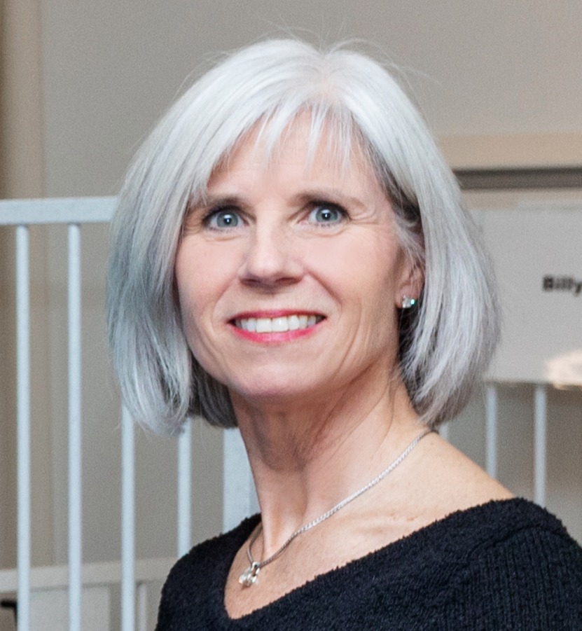 Debbie Decaire, woman with short silver hair wearing black top and smiling, headshot