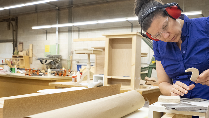 female student sanding components of a wood working project in a cabinet making workspace.