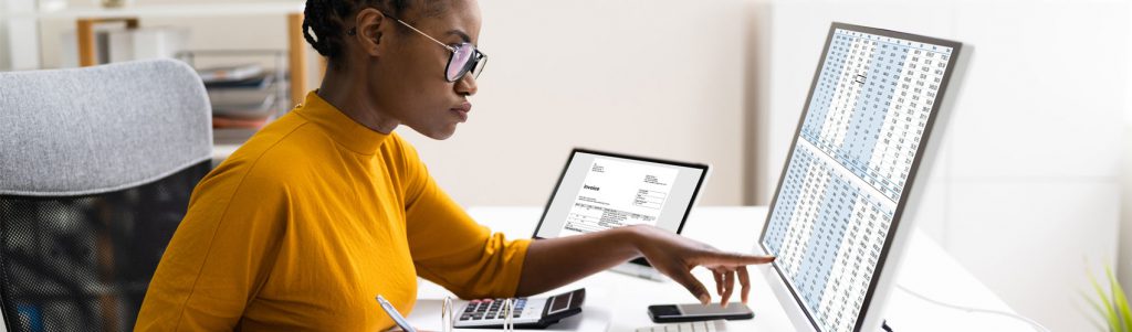 Accounting student with brown hair, glasses, a beard and plaid, collared shirt sitting at a desk looking at a computer screen