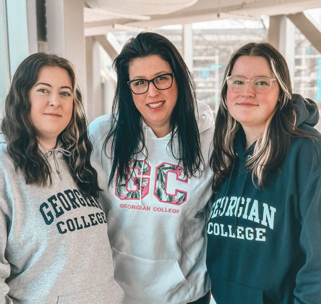 Three people each wearing Georgian College sweatshirts stand together and smile. 