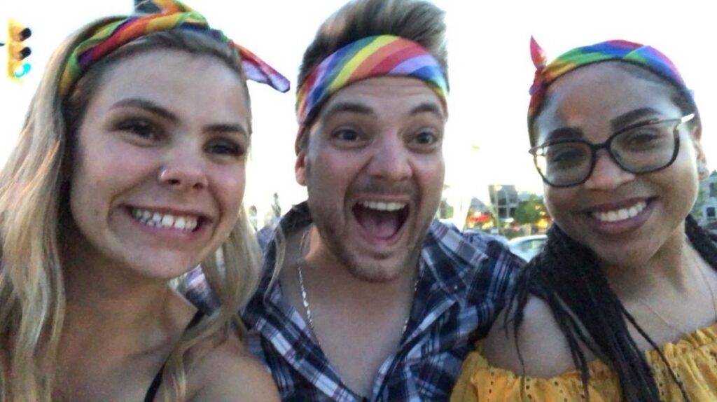 Three people each wearing a rainbow headband take a smiling selfie together.