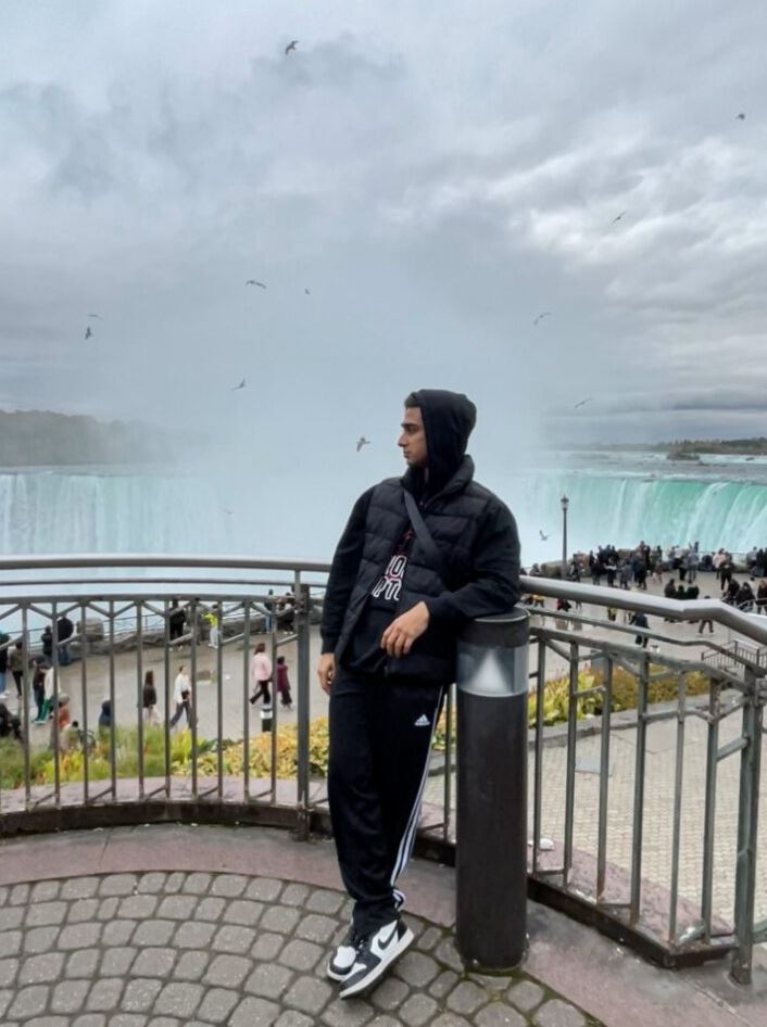 A person leaning against a railing with Niagara Falls in the background. 