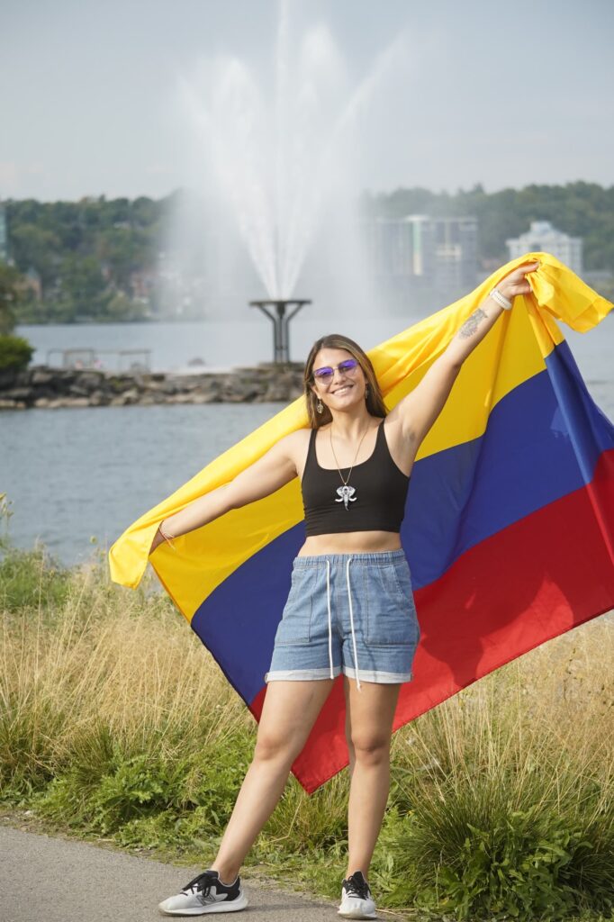 A person stands outside and holds up a yellow, blue and red Colombia flag behind them.