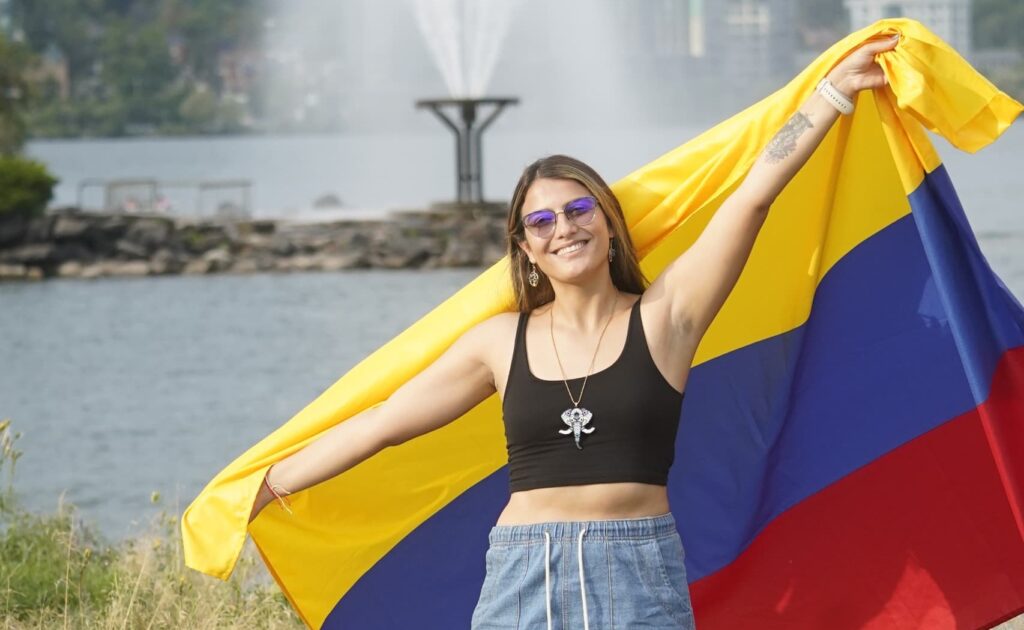 A person stands outside and holds up a yellow, blue and red Colombia flag behind them.