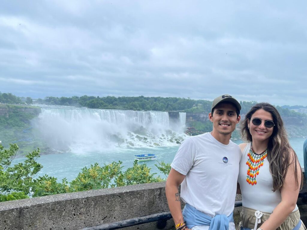 Two people smile from a viewing platform with Niagara Falls in the background. 