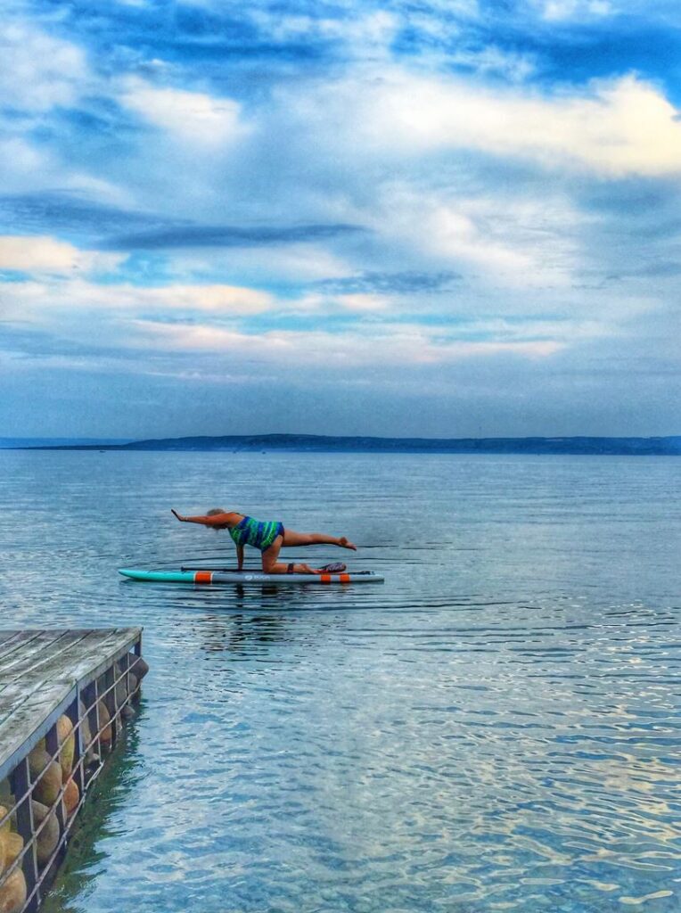 A person holds a yoga pose on a stand-up paddleboard on a lake.