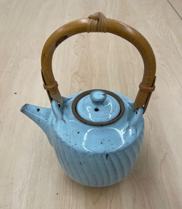 A blue ceramic kettle with a wooden handle sits on a desk.