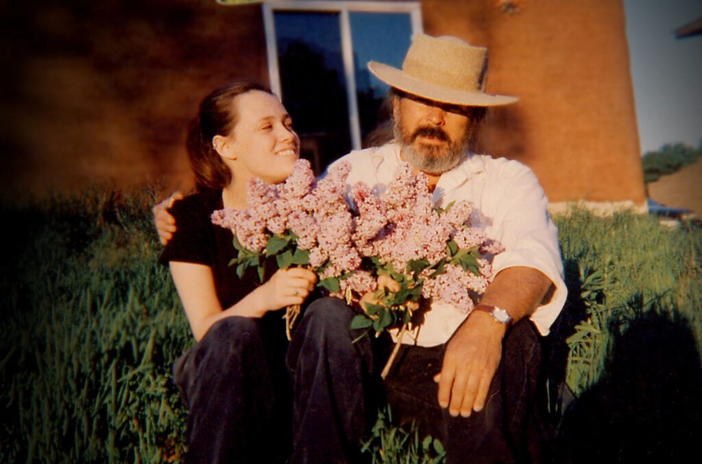 Two people sit outside together and hold a large bouquet of lilacs.