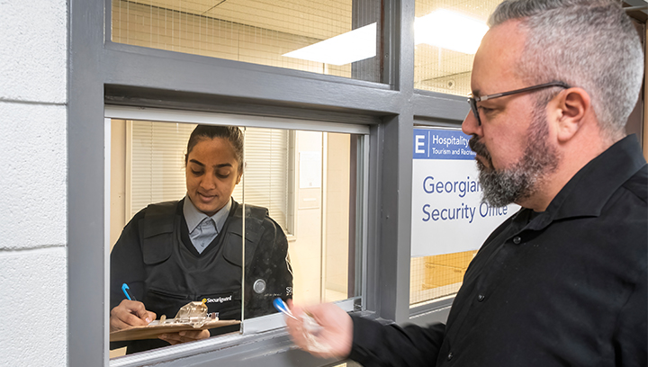 a student turning in a found item to a security guard through a service window at the Security Office at the Georgian College Barrie Campus