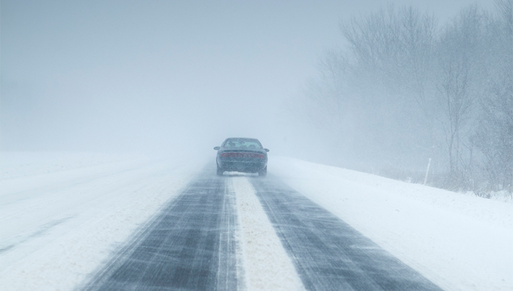 A snow-covered highway with a single driving car on a winter day