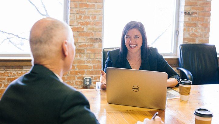 A career consultant sitting at a desk with a laptop and coffee cup, while smiling and chatting with an employer connection