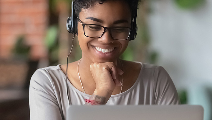 Person wearing headphones and glasses who is smiling while looking at a laptop screen
