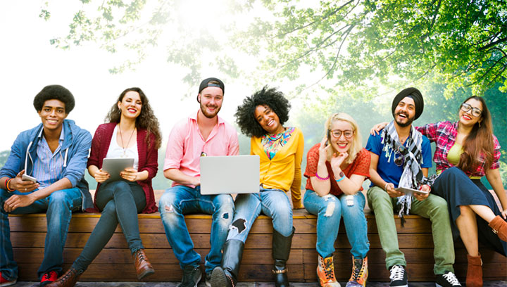 A group of people sitting on a wooden bench outside with trees and a sunlight in the background