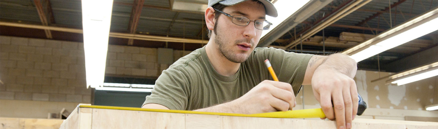 A Carpentry and Renovations Technique student in a workshop using a tape measure and pencil to mark a piece of wood