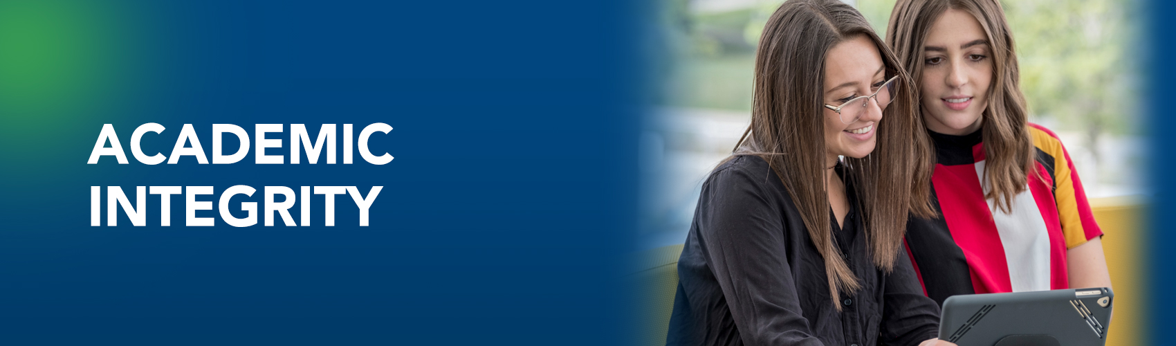 Two female students discussing while looking at a tablet device. Banner for Academic Integrity page.