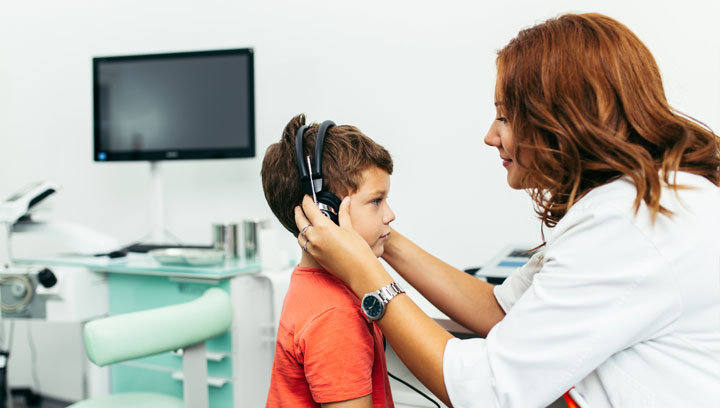 Communicative Disorders Assistant holding earphones over a young child's ears in a hearing clinic setting