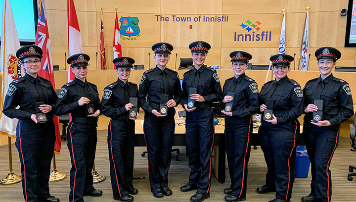 Auxiliary officers standing in police uniforms while holding badges at the South Simcoe Police Service ceremony, Town of Innisfil
