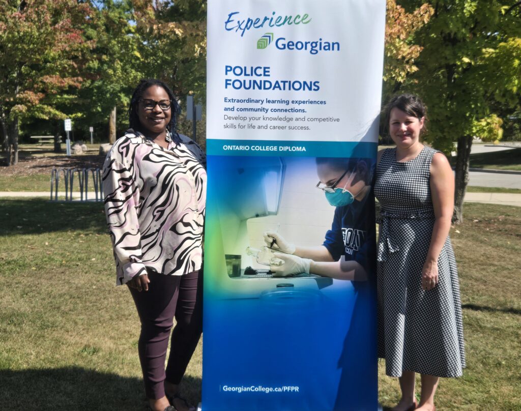 Two people stand outside on either side of a poster reading: Experience Georgian. Police Foundations.