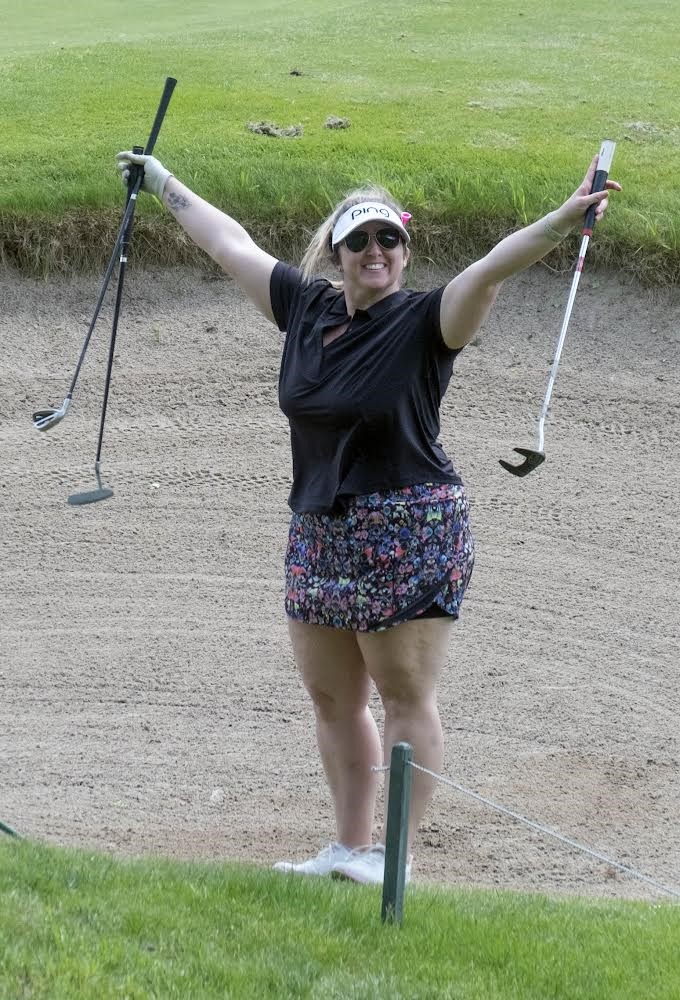 A person stands on a golf course and holds up several golf clubs.