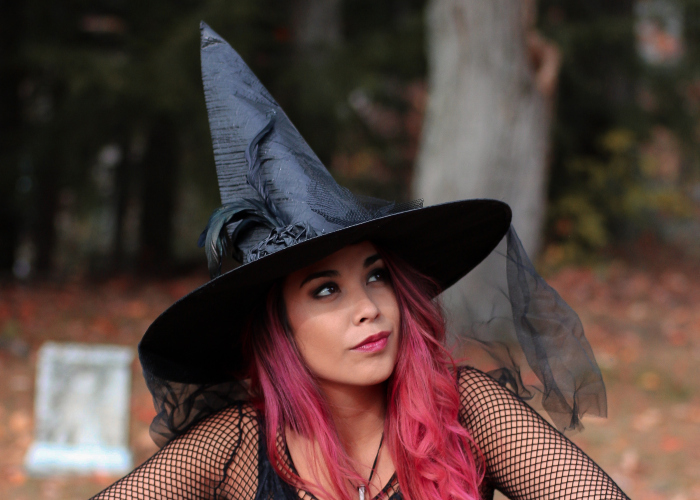 woman with pink hair and pink lipstick wearing a black with hat and a fishnet-sleeved top