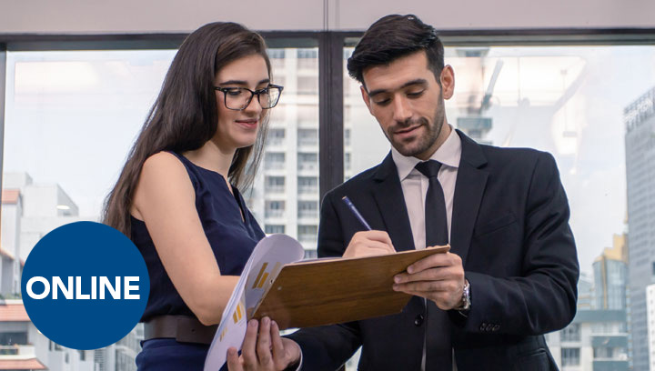 Person in a suit and tie holding out a clipboard with paperwork while a colleague wearing glasses and a dress signs in pen