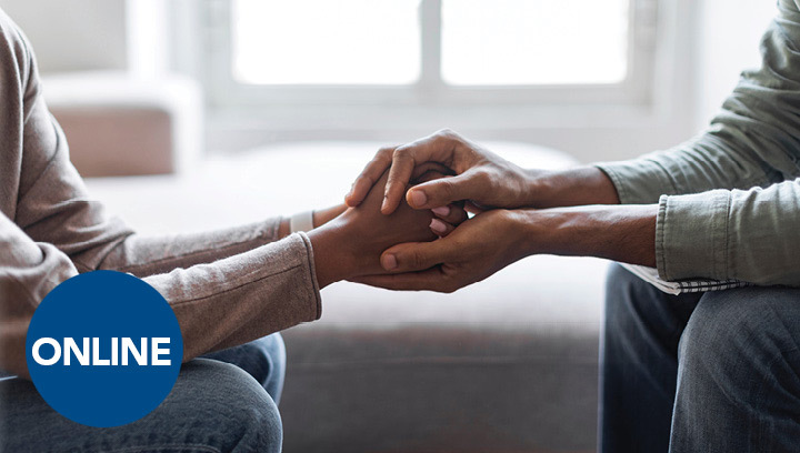 A grief counsellor sitting across from a client with their hands wrapped around the client's hands, offering support with the loss of a loved one