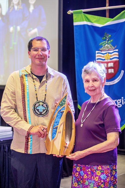 Georgian alumnus Chris and Visiting Elder Ernestine hold up the Eagle Feather that will be used in all convocation ceremonies moving forward