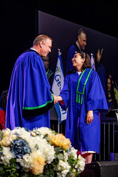 President Weaver shaking the hand of a grad on stage at convocation, both in Georgian blue gowns