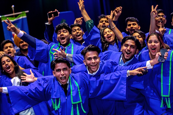 Group of happy grads smiling, cheering and hands in the air, all wearing a Georgian blue gown