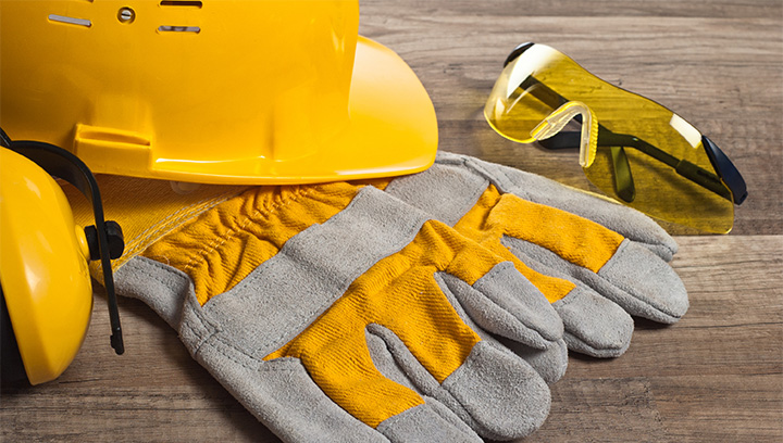 Safety gear, including a yellow hard hard, yellow safety goggles, yellow ear muffs and grey and yellow work gloves
