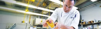 Culinary professor Anthony Borgo wearing a chef's uniform inside the culinary lab grating cheese over a pasta dish