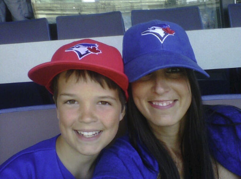 A selfie of an adult and child each wearing Toronto Blue Jays hats, smiling in the stands.