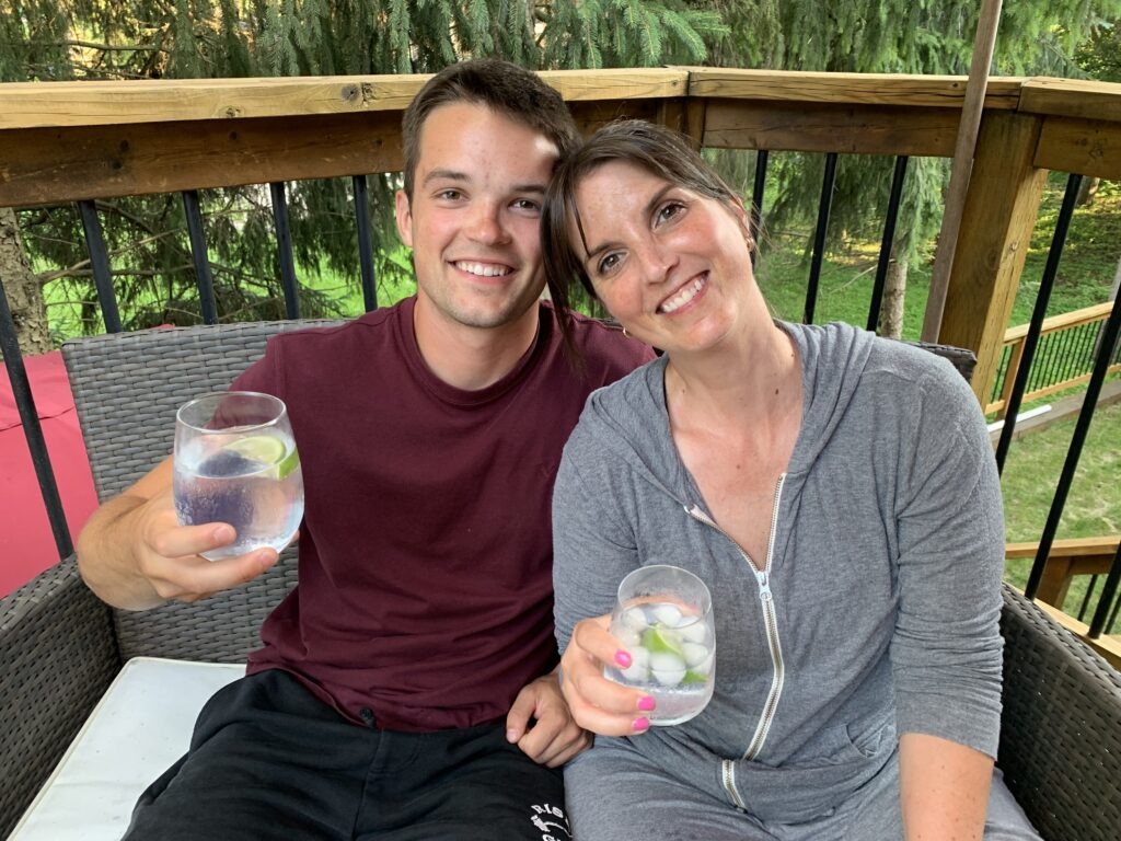 Two people sit beside each other on a patio couch and each hold up drinking glasses. 